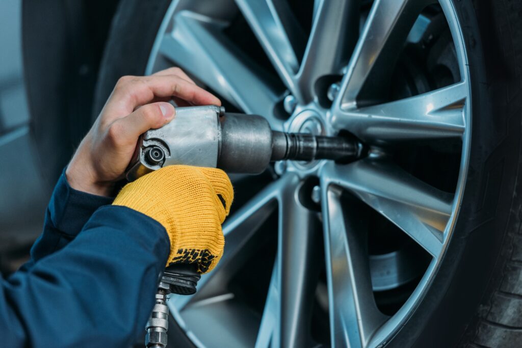 Cropped shot of automechanic unscrewing tire bolts on a lifted up car at a repair shop.