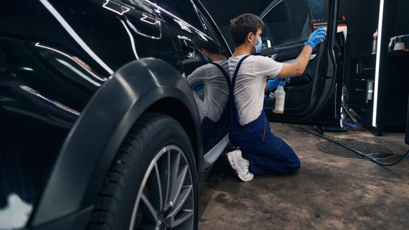 Man in repair workshop washing car window during car valeting
